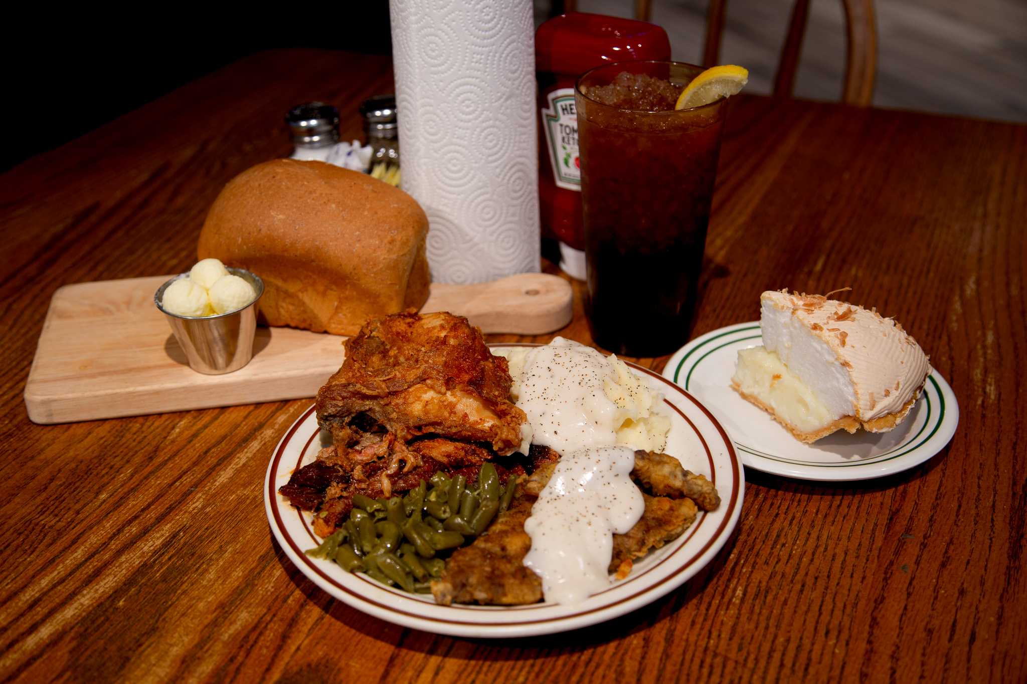 A plate from Sam's buffet with fried chicken, brisket, chicken-fried steak with cream gravy, mashed potatoes and green beans, served with a loaf of homemade bread, iced tea and a slice of coconut cream pie